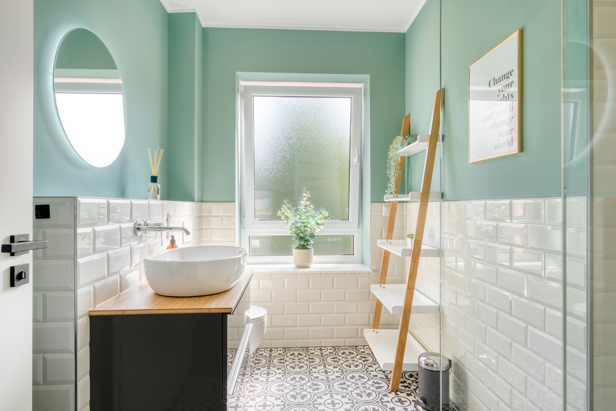 Modernes Hotelbad mit mintgrünen Wänden, Waschbecken auf Holzkonsole und hellem Tageslicht