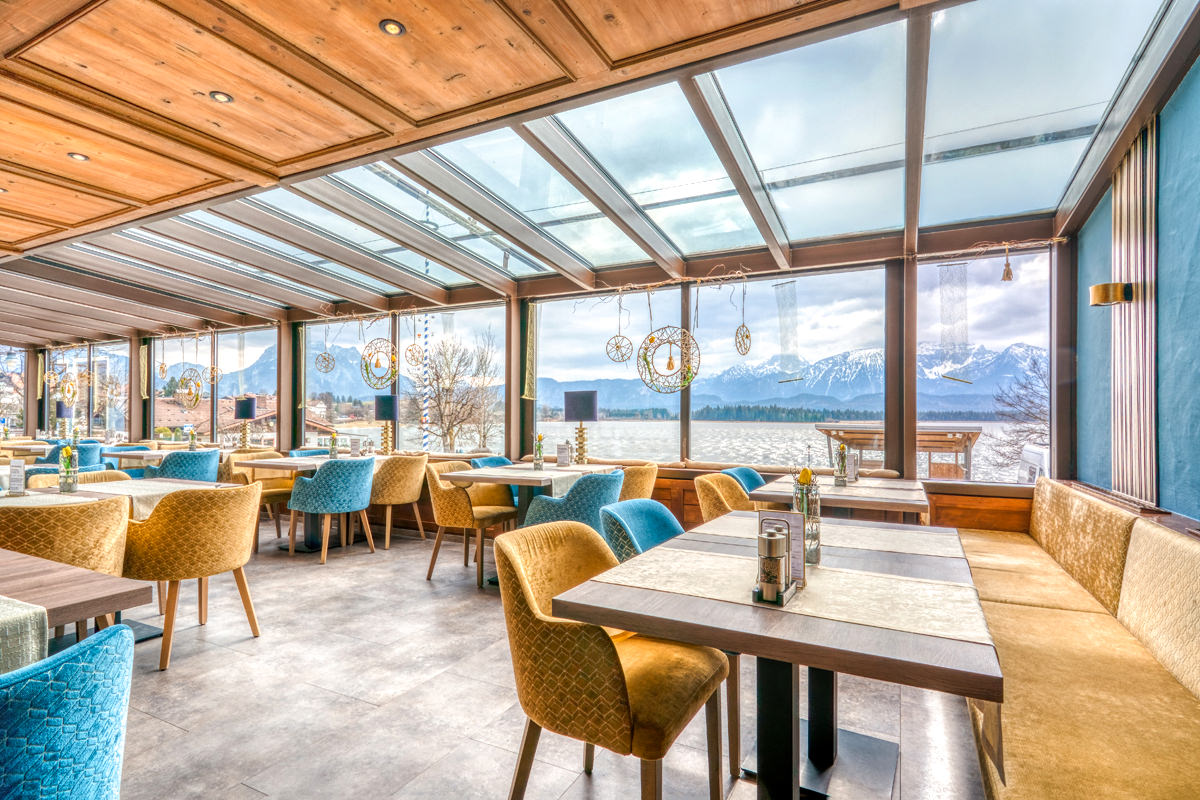 Hotelrestaurant mit großen Panoramafenstern und Blick auf See und Berge